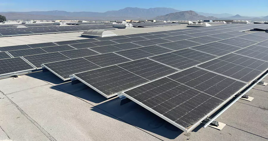 Photo of multiple rows of solar panels on top of an industrial warehouse with mountains in the distance