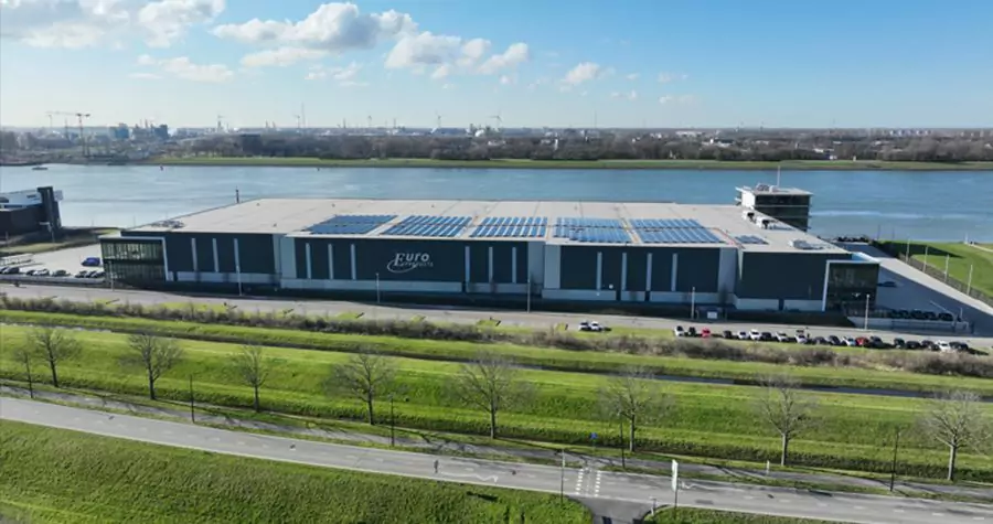 Large two-level European industrial warehouse with rooftop solar panels next to a river and highway